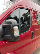 Red rv rental van exterior, featuring the driver's side door, tinted window, and a black side mirror with a turn signal.