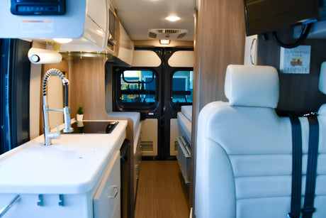 Bright RV rental interior with kitchen, rear doors, and white seating. Adventure awaits in this camper van.