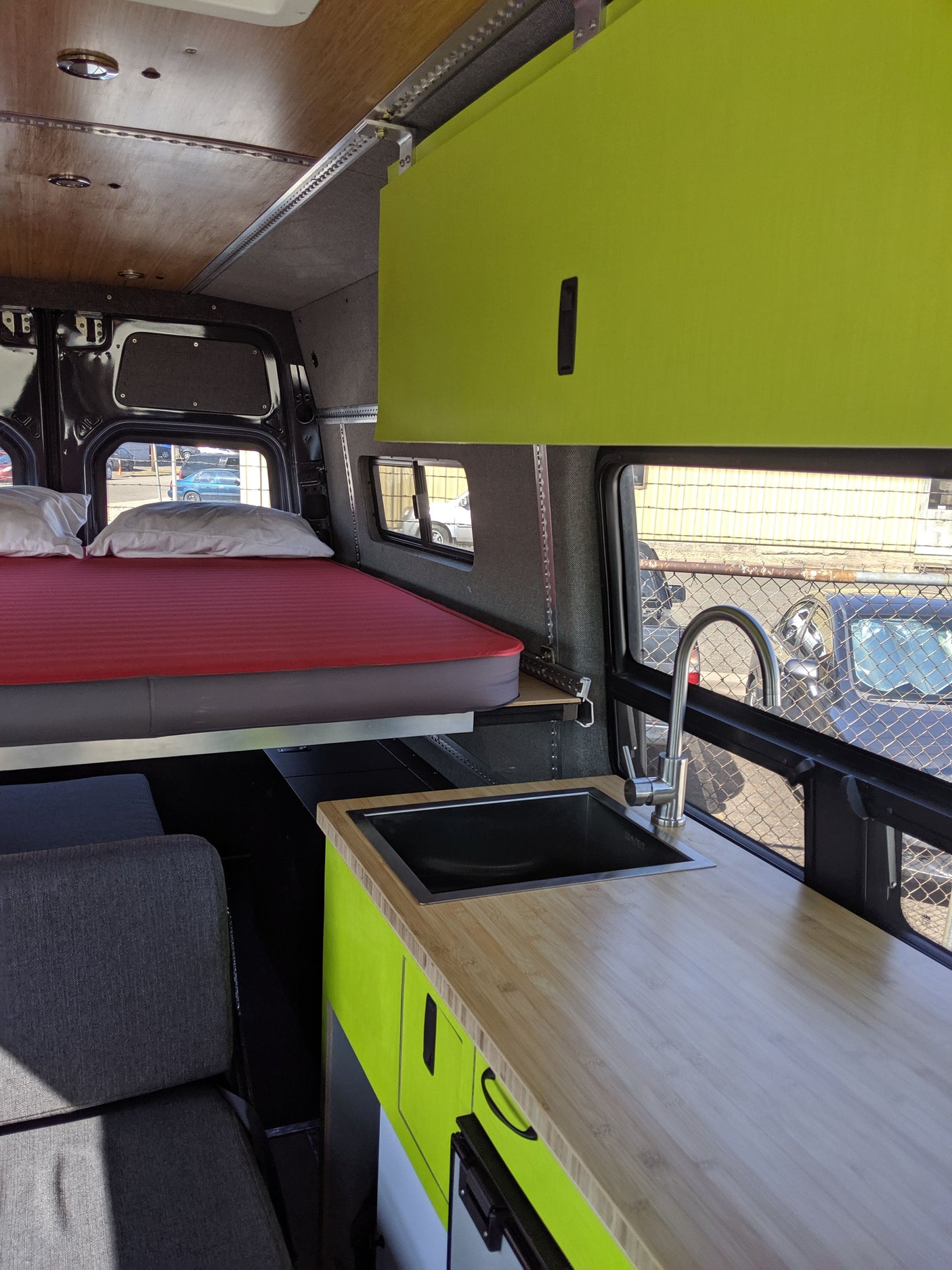 Rv rental van interior: lime green cabinets, kitchen with sink, bed, and grey seating area. A well-equipped camper van.
