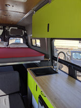Rv rental van interior: lime green cabinets, kitchen with sink, bed, and grey seating area. A well-equipped camper van.