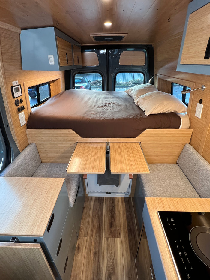 Spacious rv rental interior: bed, cozy seating with pull-out tables, integrated kitchen, and overhead storage.