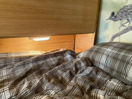 Cozy RV rental bunk bed with plaid bedding and built-in reading light, offering comfort on your journey.
