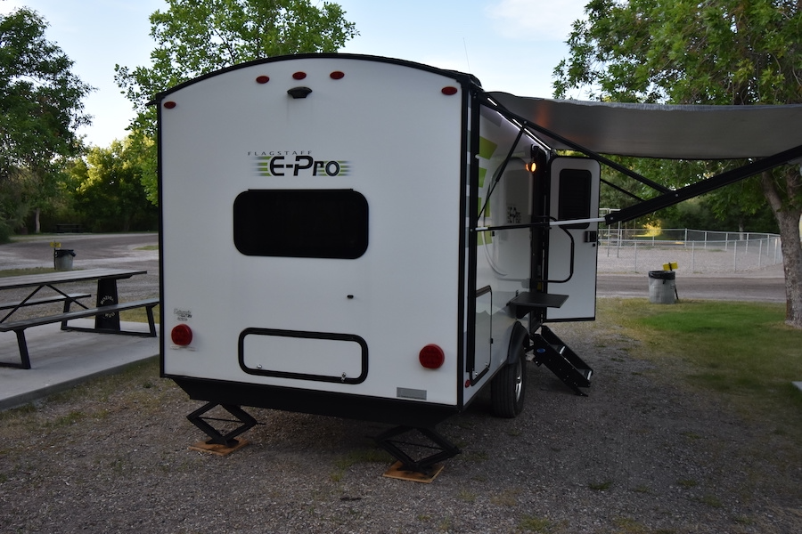 White Flagstaff E-Pro RV rental travel trailer at a gravel campsite. Awning extended, jacks down, ready for camping. — photo 9