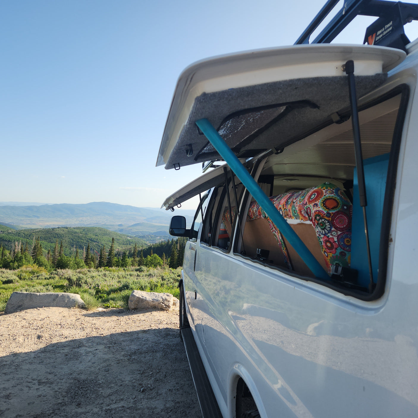 RV rental adventure: A white van's open side reveals a cozy interior, overlooking a vast mountain landscape.
