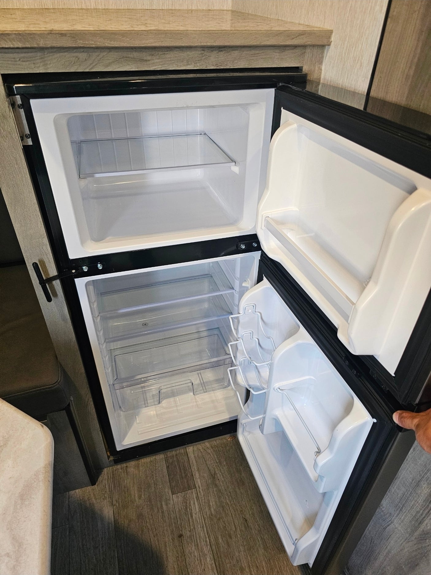 Open, clean RV rental fridge and freezer with empty shelves and door compartments, ready for your trip.