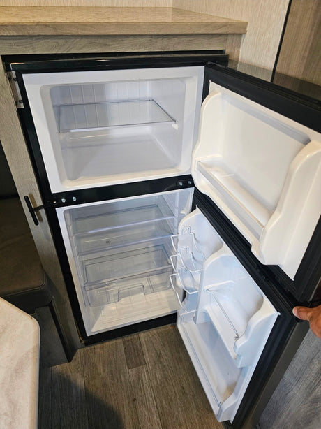 Open, clean RV rental fridge and freezer with empty shelves and door compartments, ready for your trip.