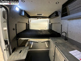RV rental interior featuring a raised bed with black mattress, kitchenette with sink, and sleek gray finishes.