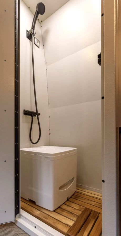 RV rental wet bath: compact shower with handheld head, modern toilet, and slatted wood floor for a convenient mobile bathroom.