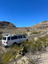 White RV rental van parked roadside on a winding desert mountain road with a distant tunnel. Ideal for a scenic outdoor adventure.
