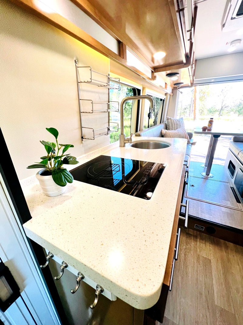 This modern RV rental features a well-appointed kitchen with a sleek countertop, sink, and stovetop, plus a cozy dining area. — photo 3