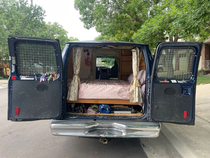  and a clear view out the back.|A custom blue camper van with open rear doors revealing a bed and organized storage inside — photo 2