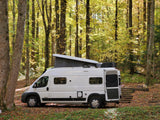 A white camper van (RV rental) with its pop-top roof open, parked in a vibrant autumn forest.