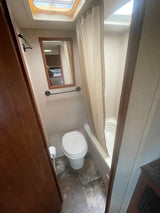 RV rental bathroom showing a toilet, tub/shower with curtain, wall mirror, and ceiling skylight for light.