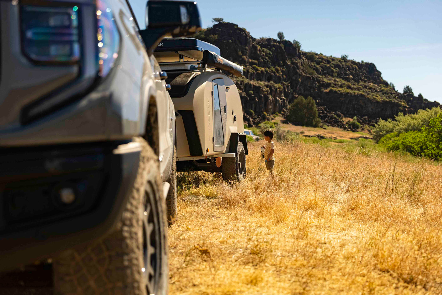 Enjoy your RV rental adventure! A child by an Escapapod camper trailer & truck in a sunny, arid landscape.