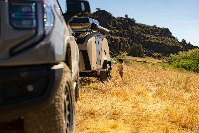  with a woman and young child outdoors.|This rugged GMC Sierra AT4X tows an Escapapod teardrop RV rental trailer through dry — photo 7