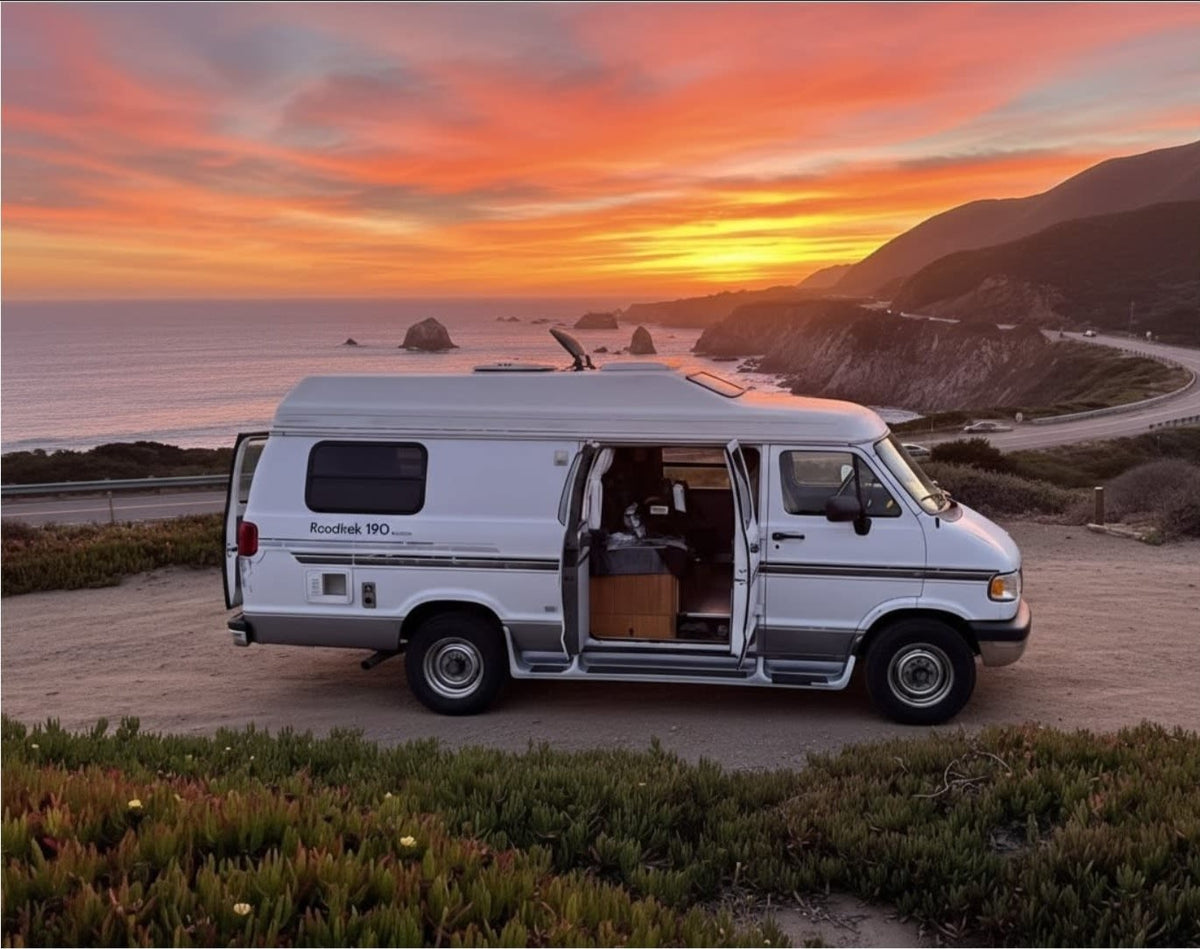 A white Roadtrek 190 RV rental camper van overlooks a vibrant orange and pink sunset over the Pacific Ocean and winding coastline.|White RV rental at a vast desert overlook