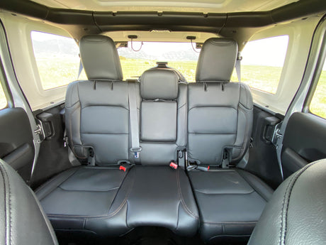 Interior of an SUV-style RV rental: black leather back seats, headrests, and scenic views of fields and mountains.