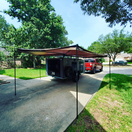 Explore with this overland camper and its attached awning, towed by a red truck in a driveway. Perfect for your RV rental adventures!