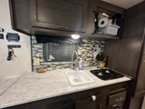 Inside an RV rental: a compact kitchen with sink, two-burner stove, and overhead storage.