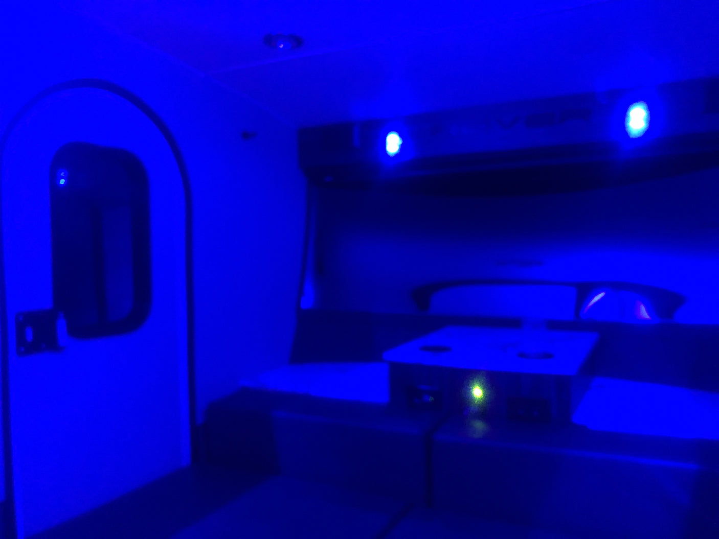 Cozy blue-lit RV rental interior featuring a door, comfortable seating, and a modern charging station.
