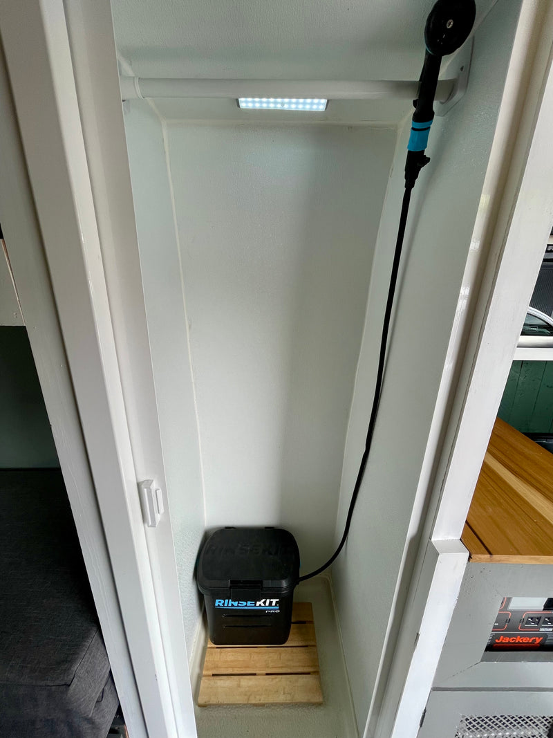 RV rental's compact shower space with a portable RinseKit, wooden mat, LED light, and wall-mounted shower head. — photo 20