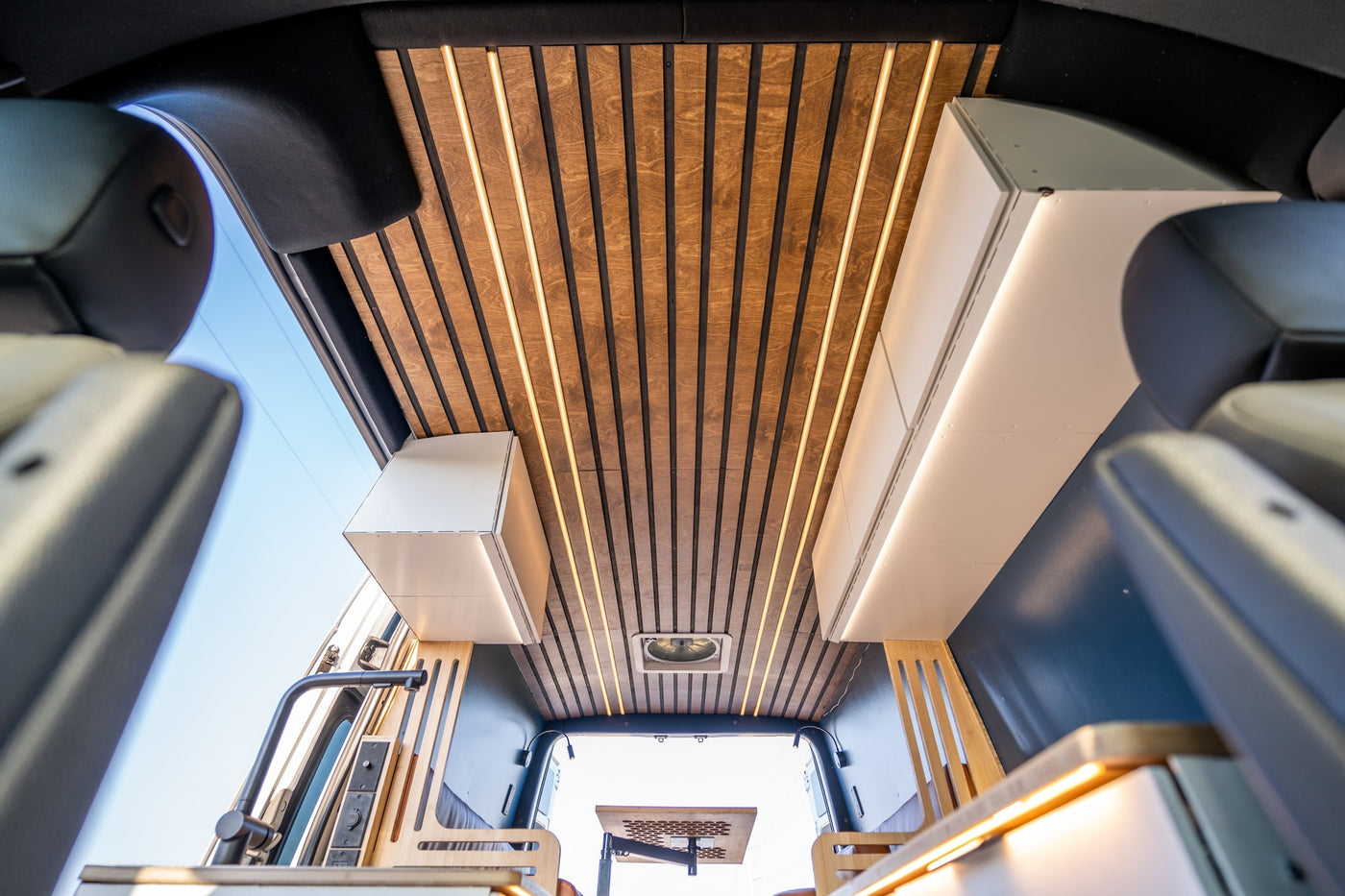View from front seats inside a modern rv rental: wood-slatted ceiling with bright lights & sleek cabinets. — photo 8