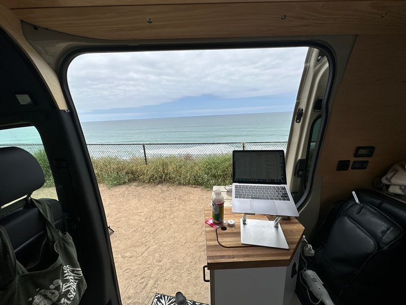 Ocean view mobile office in an RV rental. Laptop on a wooden desk inside the van, overlooking the sea with a fence. — photo 5