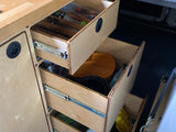 Organized plywood drawers in an RV rental, with kitchen items like plates and pots, showing efficient storage for travel.