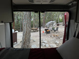 Cozy view from an RV rental, looking out at a peaceful campsite with a warm campfire, trees, and rocks. Perfect camping!