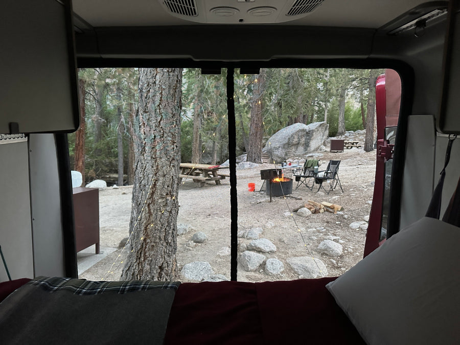 Cozy view from an RV rental, looking out at a peaceful campsite with a warm campfire, trees, and rocks. Perfect camping!