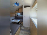 Inside a modern RV rental: view of the dinette with gray cushions, a ceiling fan, and light wood flooring.