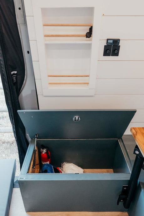 RV rental interior features: an open storage box with a fire extinguisher, custom shelving, and control panels.