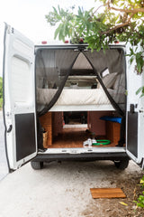 Open back of an RV rental reveals a converted van interior with bed, storage, and mesh screen for comfortable travel.