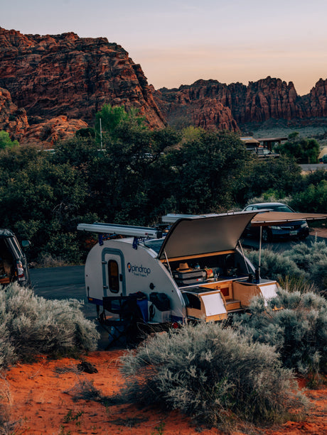 An Opindrop teardrop rv rental is set up in a red rock desert campsite with an open kitchen, perfect for nature travel.