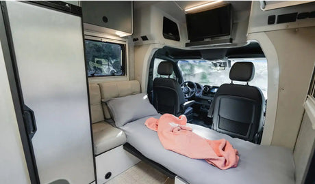 Modern RV rental interior showing compact living space, comfortable bed, fridge, and front cabin. Ideal for mobile travel.