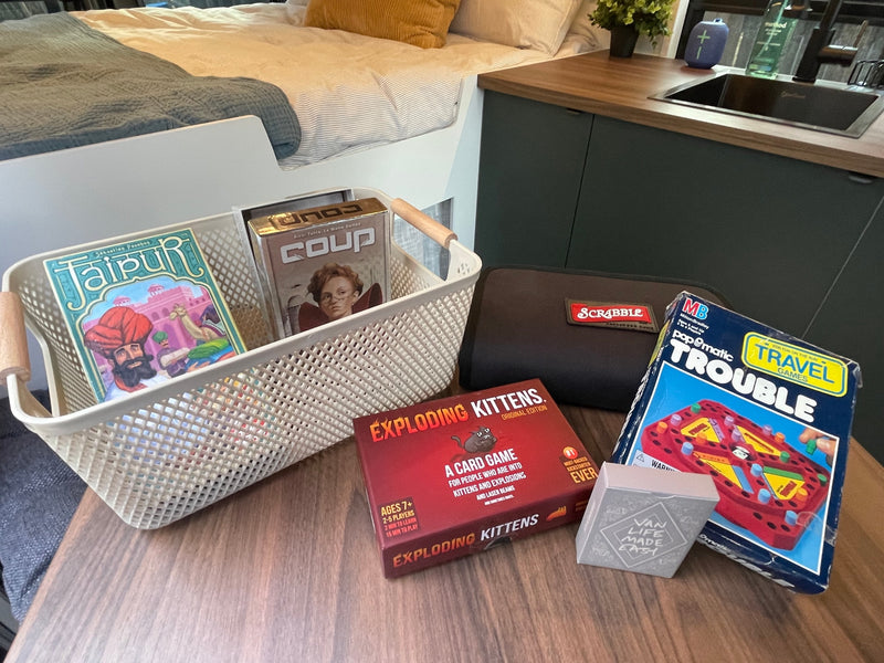 An RV rental's cozy setup: a basket of games (Jaipur, Coup), Exploding Kittens, Scrabble, and Travel Trouble, next to a bed & kitchenette. — photo 18