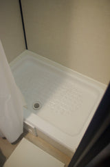 Clean white shower stall with a clear non-slip mat and drain, ideal for an RV rental.