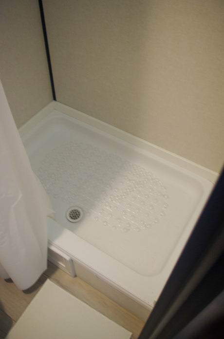 Clean white shower stall with a clear non-slip mat and drain, ideal for an RV rental.