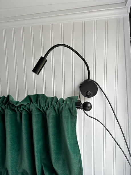 Cozy RV rental interior featuring white beadboard walls, a black gooseneck reading lamp, and soft green curtains.