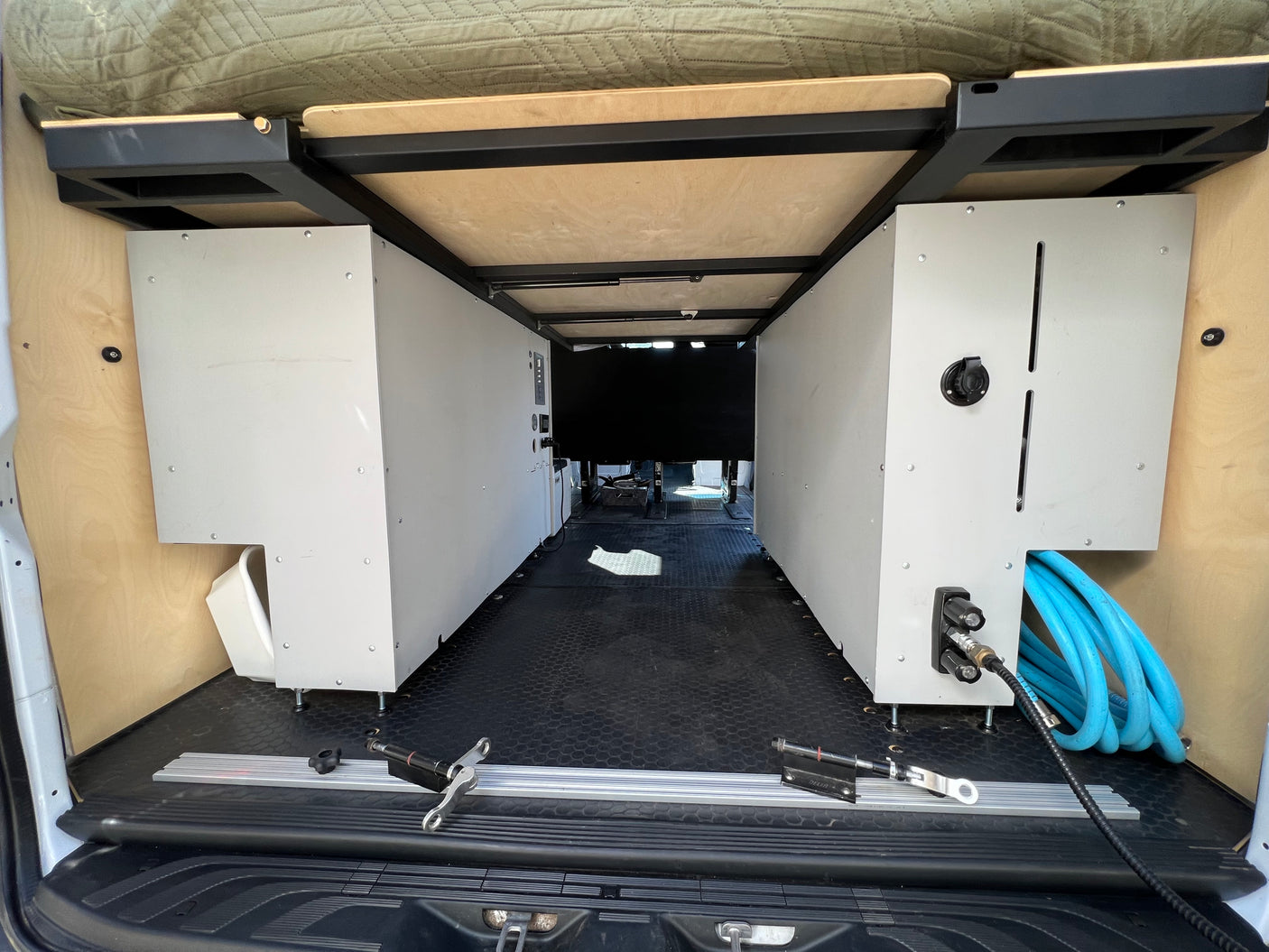 RV rental camper van interior: organized storage modules, overhead bed platform, and utility connections in the rear.
