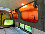 Efficient rv rental space: comfortable bed & organized overhead storage with bright orange interior and open compartments.