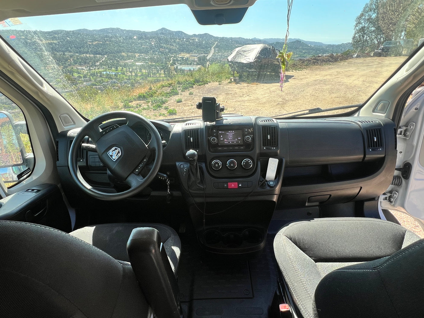 Inside an RV rental van: driver's perspective with dashboard, steering wheel, and a scenic view of mountains and hills outside.