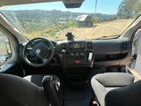 Inside an RV rental van: driver's perspective with dashboard, steering wheel, and a scenic view of mountains and hills outside.
