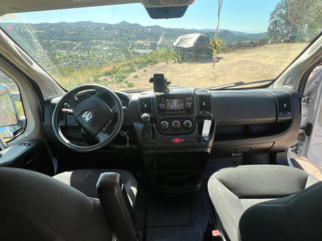 Inside an RV rental van: driver's perspective with dashboard, steering wheel, and a scenic view of mountains and hills outside.