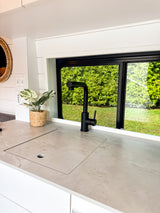 Bright RV rental kitchen featuring a covered sink, black faucet, and lush outdoor view through the window.