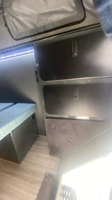 Inside an RV rental, this view highlights compact interior storage with latches, bright LED lighting, and a grey upholstered seating/bed area.