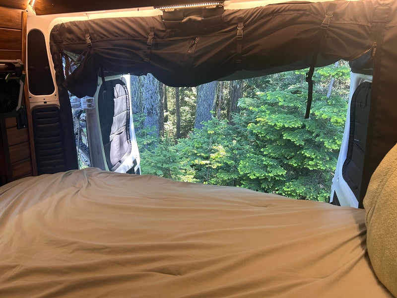 Wake up to nature! This cozy rv rental features a comfy bed and open back doors revealing a vibrant forest view. — photo 13