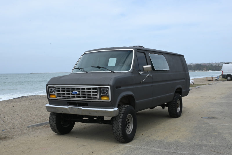 Adventure-ready dark gray Ford van parked by the ocean, ideal as an RV rental for beach trips. — photo 1
