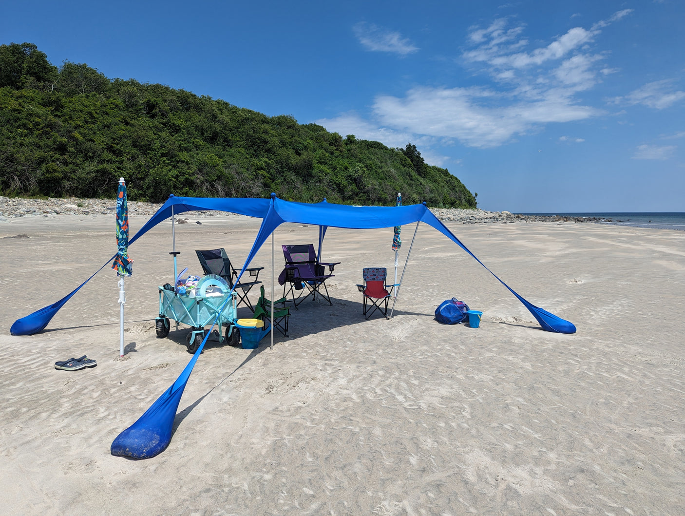 Relaxing under a blue sunshade with chairs on a sunny beach, perfect after an RV rental adventure.
