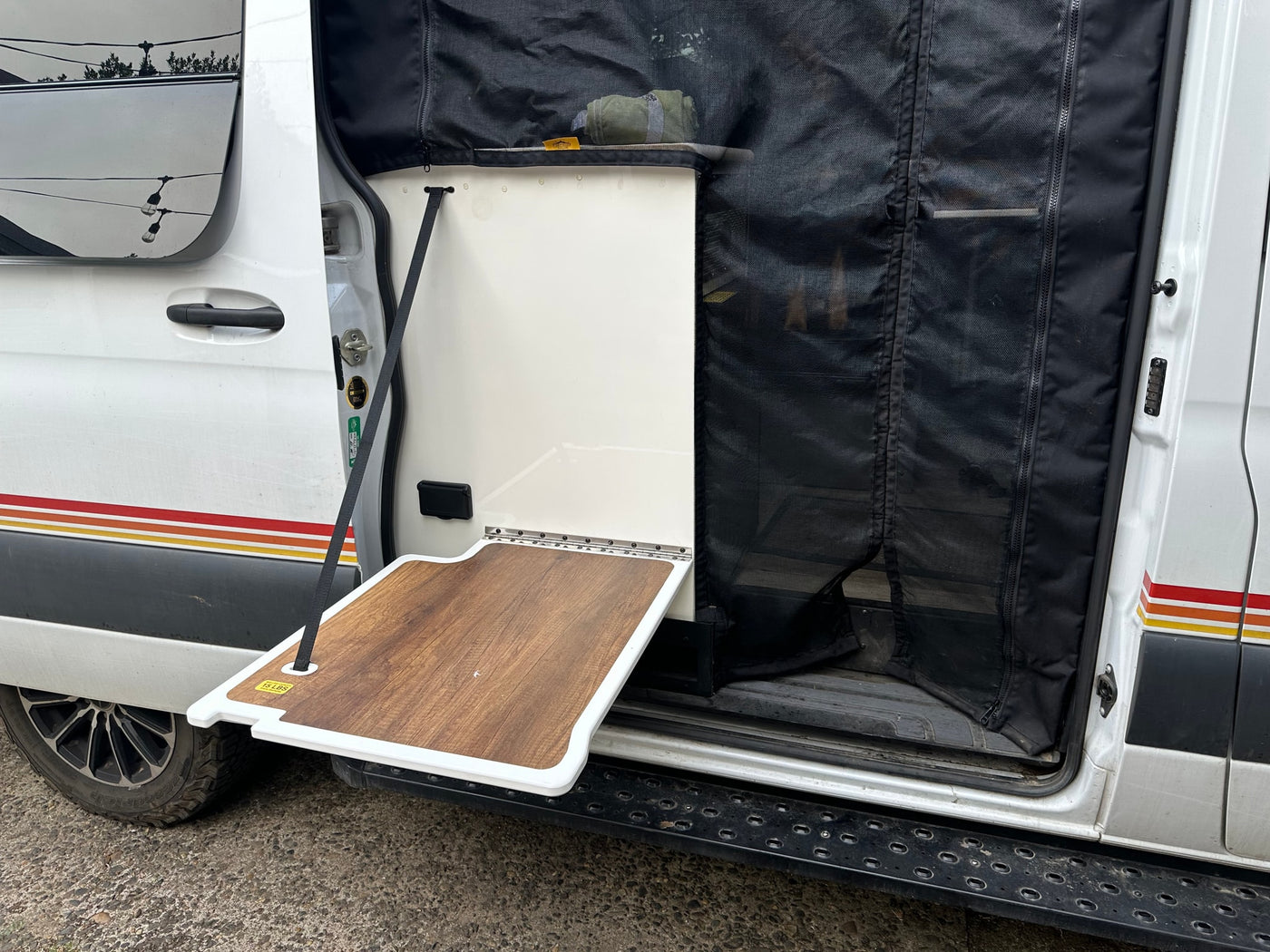  celebrating amidst striking rock formations.|A dirty white rv rental camper van with adventure gear parked lakeside before snowy mountains under a cloudy sky.|This RV rental features a convenient side door with a fold-down — photo 18